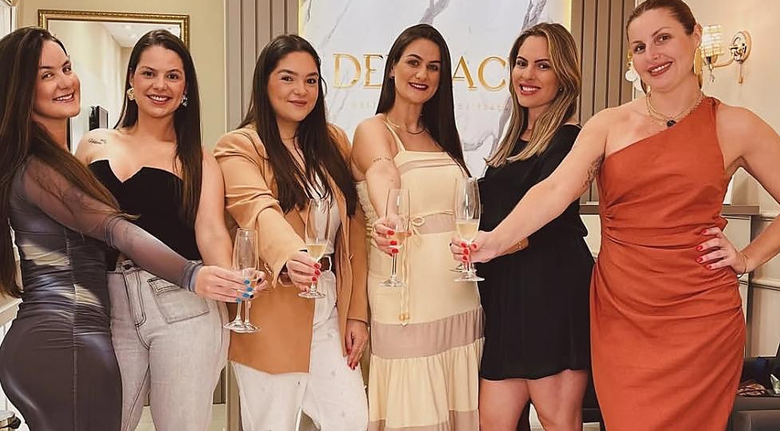 As seis profissionais da Delicacy reunidas em frente ao logo da clínica